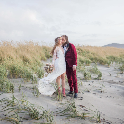 Bride and groom kiss among tall beach grass on the dunes